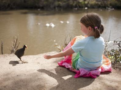 Girl sits by a river looking at bird