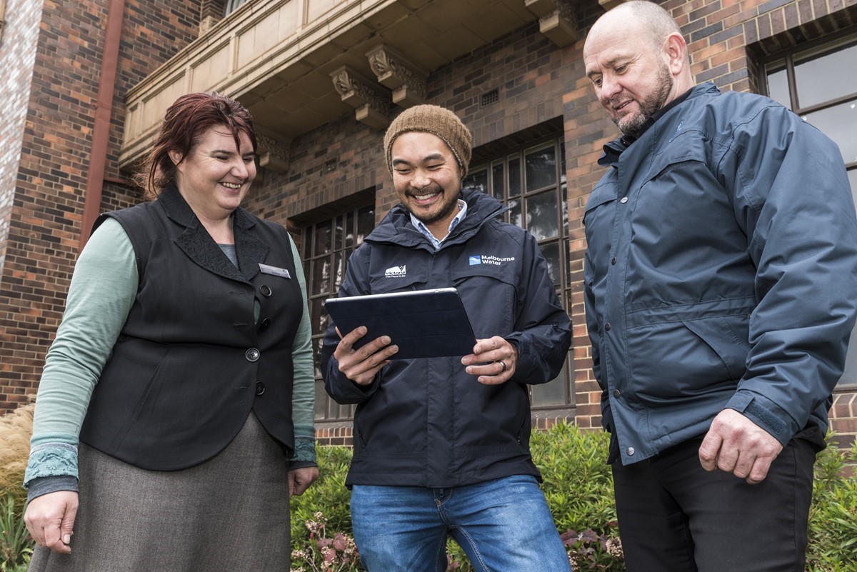 Councils and community members gather outside, they are looking at an iPad which is being used as a community engagement tool.