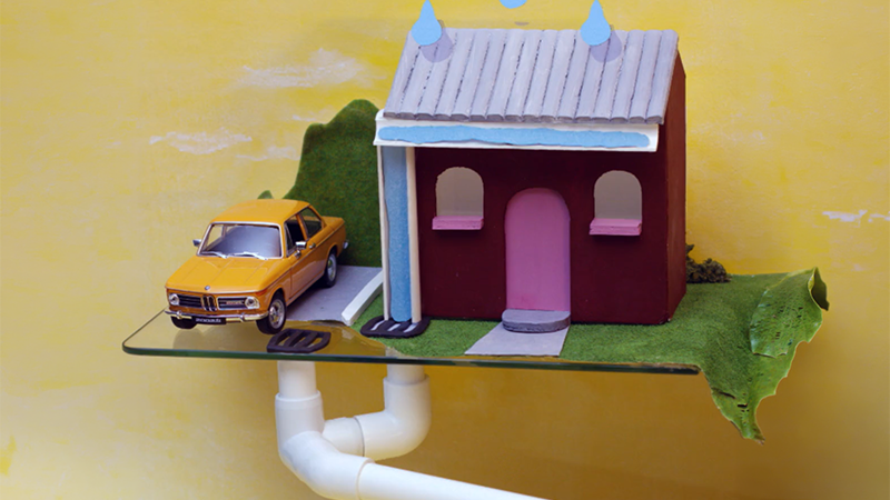 Model of a house being rained on with drains showing underneath the house