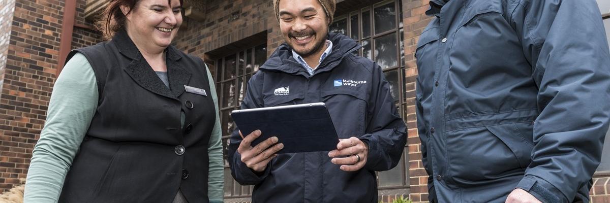 Melbourne Water staff consulting Elster Creek councils and community members Councils and community members gather outside, they are looking at an iPad which is being used as a community engagement tool.