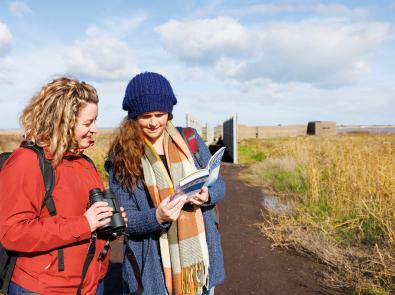 Two women in the outdoors looking at birding book and holding binoculars