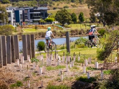 Two cyclists along an urban river with plantings in the foreground