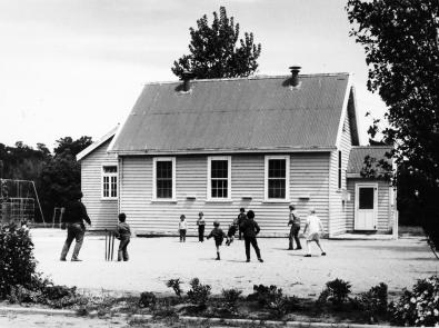 Black and white photograph of children playing in a yard in front of a small wooden building