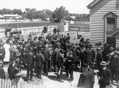 Black and white photograph of group of people in suits outside a weatherboard building