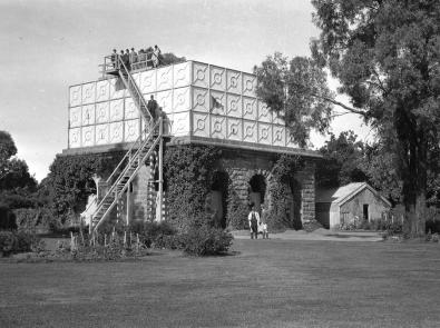 Black and white photograph of water tower covered with ivy, with a group of people standing on top