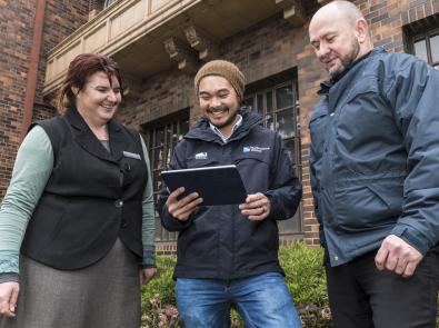 Councils and community members gather outside, they are looking at an iPad which is being used as a community engagement tool.