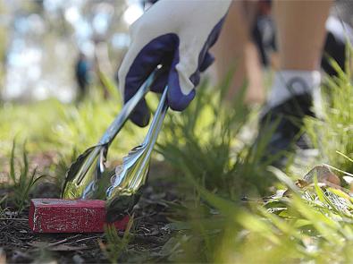 Person wearing gloves uses a pair of tongs to pick up rubbish from the ground