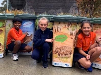 Primary school students crouch next to rubbish bins with custom of animals that say "bin it for me!"