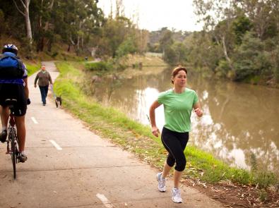 Recreation along waterway Jogger, cyclist and dog walker on shared path along creek