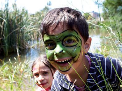 Two children, a boy with face painted as a frog, smiling amongst his local waterway