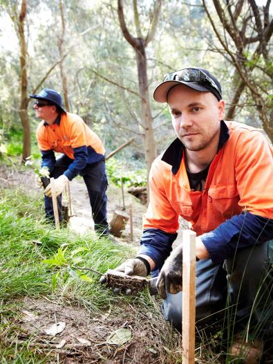 Two Melbourne Water employees planting vegetation