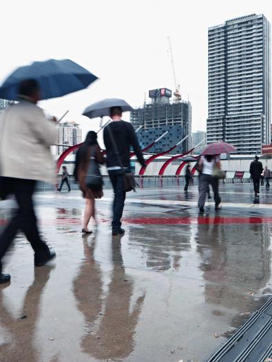 People walking down a concrete concourse carrying umbrellas