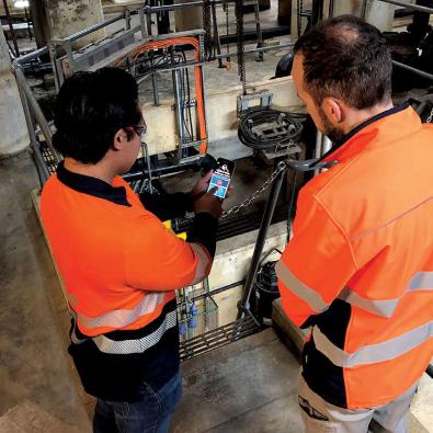 An employee uses the confined space mobile app at a work site while another looks on