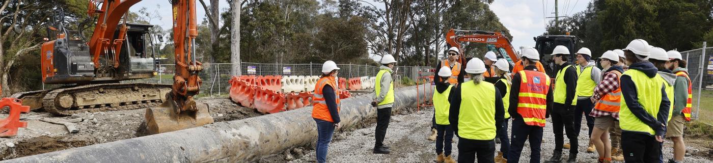 People in hi-vis vests stand in front of pipeline