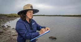 A woman standing with a notepad near water