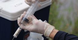 Close up of gloved hands using a syringe to collect water samples from a river.