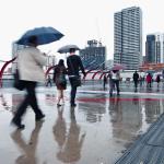People walking down a concrete concourse carrying umbrellas