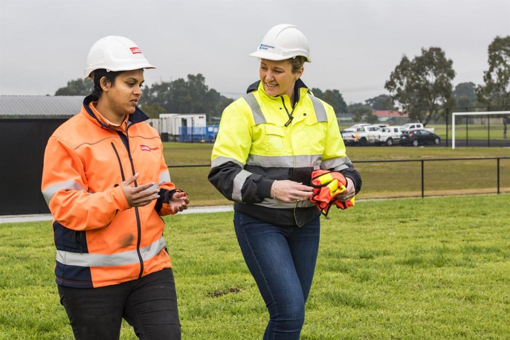 Two women in hi-vis and hard hats walk side by side