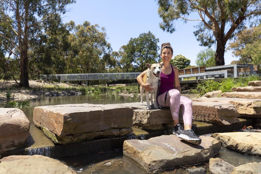A woman and a dog sitting on a rock in a creek