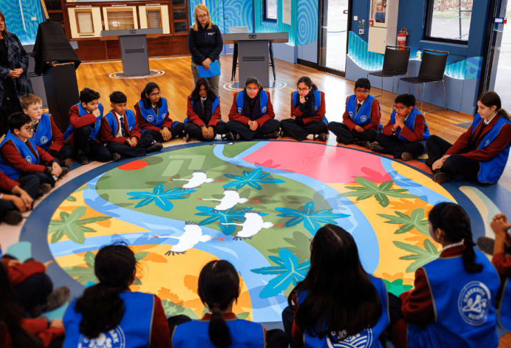 Circle of students sitting on the floor looking at a projection