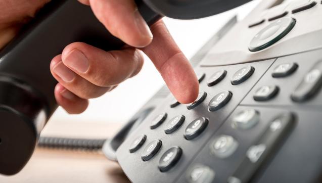Person holding phone receiver dialling number