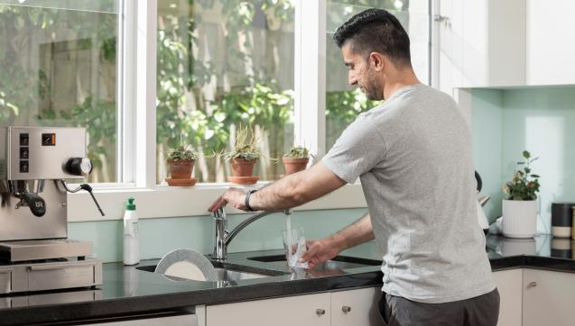 Man turning on kitchen tap to get a glass of water