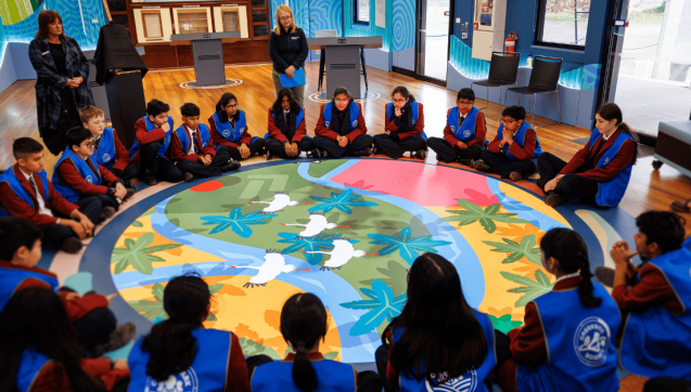 Circle of students sitting on the floor looking at a projection