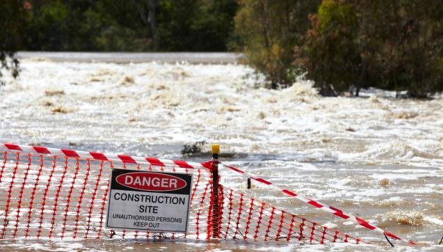 Overflowing river with danger sign washed away by floodwaters
