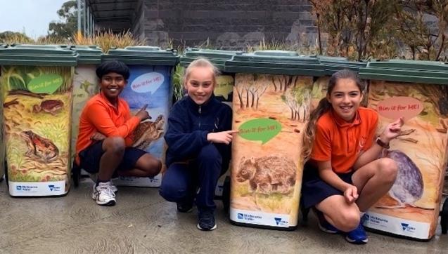 Primary school students crouch next to rubbish bins with custom of animals that say "bin it for me!"