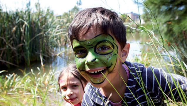 Two children, a boy with face painted as a frog, smiling amongst his local waterway
