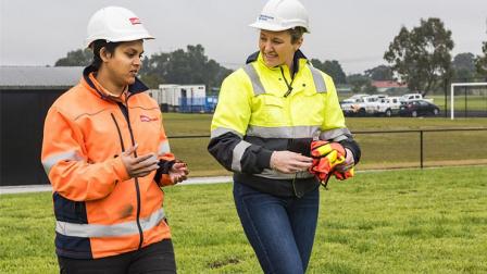 Two women in hard hats and high-visibility workwear talk at a project site