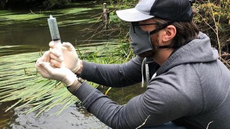 Man wearing face mask collects eDNA sample by a river