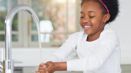Young girl washes her hands over a sink