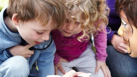 Two children inspect water bugs in a white tub.